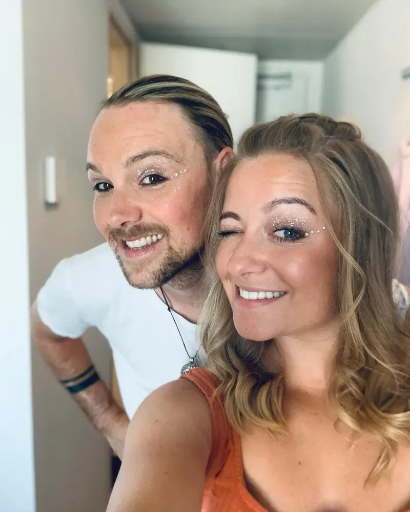 Maik und Chiara lächeln mit glitzerndem Augen-Make-up in die Kamera, Chiara zwinkert.