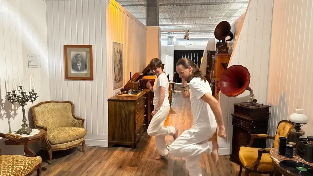 Mirja und Maik in weisser Kleidung bei einer Tanzbewegung zwischen alten Möbeln und Grammofonen während des Videodrehs.