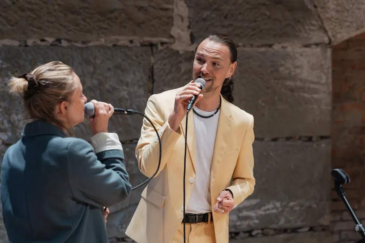 Chiara und Maik singen bei einer Hochzeit einander zugewandt mit Mikrofonen.
