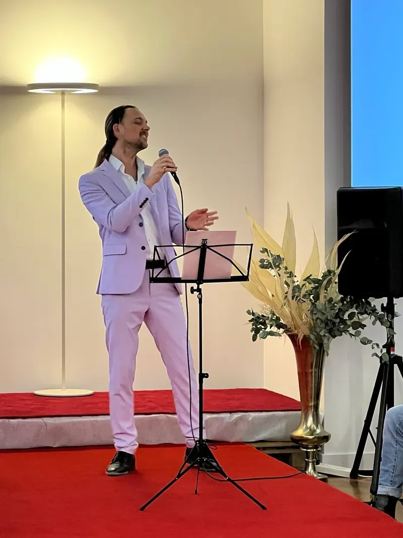 Maik im hellvioletten Anzug mit Mikrofon und Notenständer bei einem Auftritt an einer Hochzeitsmesse in Thun.
