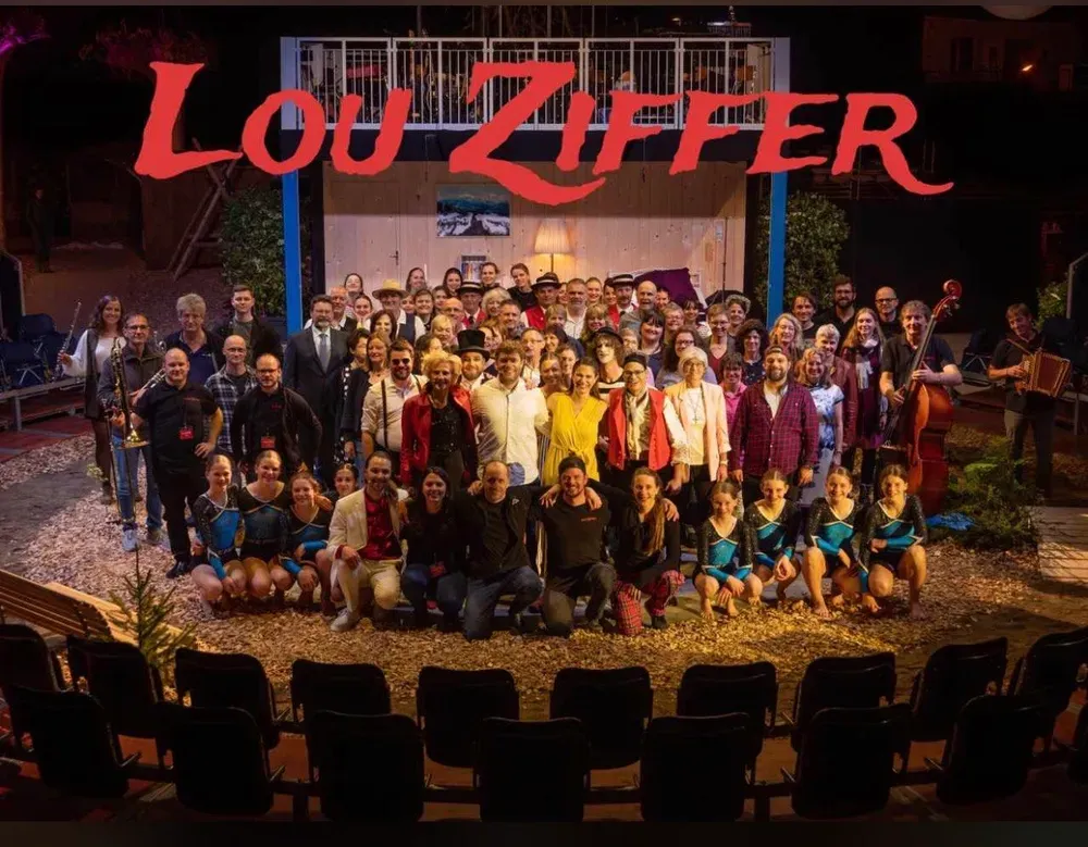 Gruppenfoto der Mitwirkenden auf der Bühne, darüber der rote Schriftzug «Lou Ziffer».