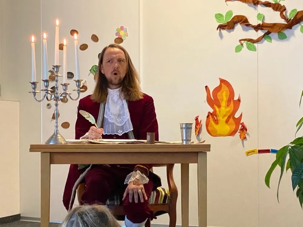 Maik in historischem Kostüm mit Schreibfeder an einem Tisch neben einem Kerzenleuchter.