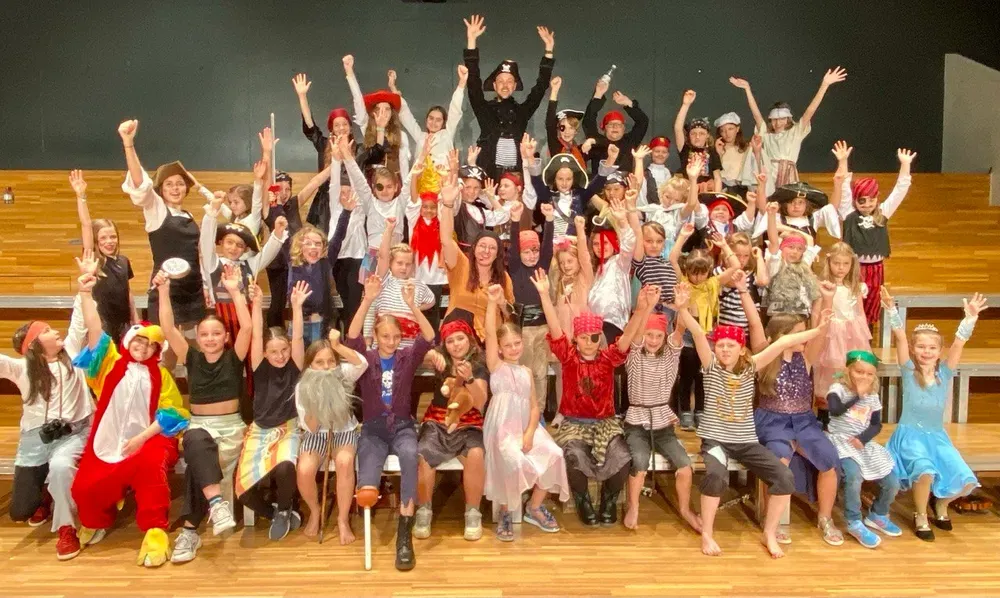 Gruppenfoto eines Projekts der Singschule Sense: Maik und eine grosse Gruppe in bunten Kostümen mit erhobenen Armen.