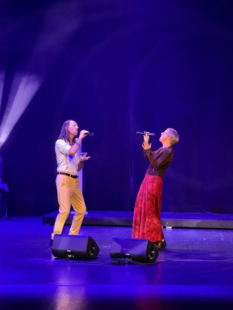 Maik und Mirja singen einander zugewandt mit Mikrofonen auf einer violett beleuchteten Bühne.