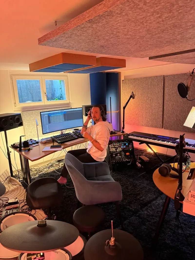 Maik mit Kopfhörern am Computer in seinem Tonstudio, umgeben von Mikrofonen und Instrumenten.